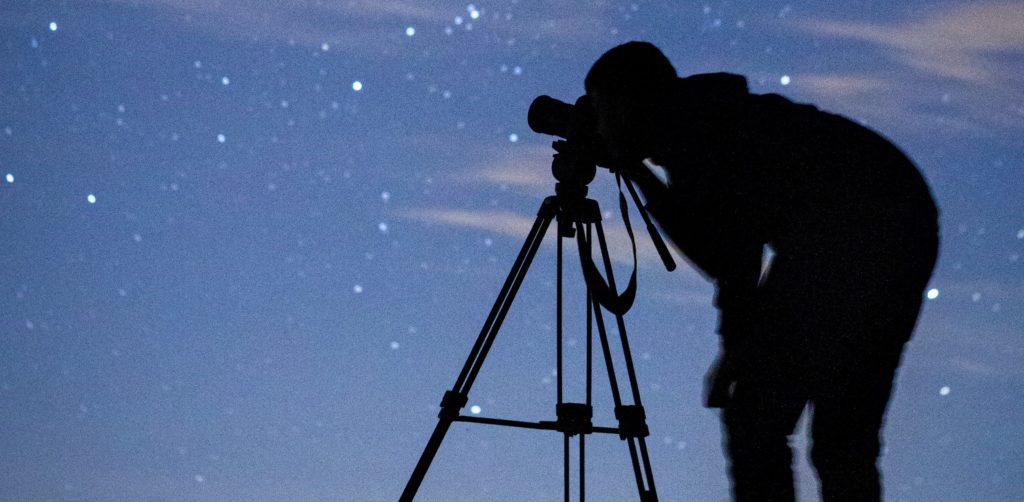 man with tripod looking at the stars